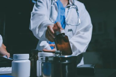 Two doctors and a female nurse meet at a table in the hospital, collaborating on medical tasks using laptops and computers