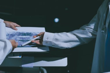 Two doctors and a female nurse meet at a table in the hospital, collaborating on medical tasks using laptops and computers