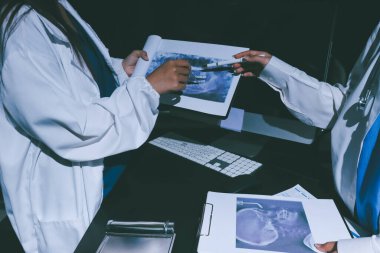 Two doctors and a female nurse meet at a table in the hospital, collaborating on medical tasks using laptops and computers