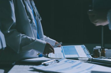 Two doctors and a female nurse meet at a table in the hospital, collaborating on medical tasks using laptops and computers