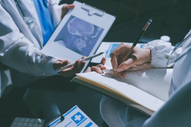 Two doctors and a female nurse meet at a table in the hospital, collaborating on medical tasks using laptops and computers