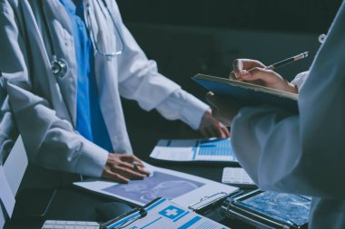 Two doctors and a female nurse meet at a table in the hospital, collaborating on medical tasks using laptops and computers