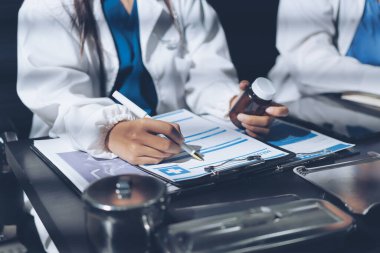 Two doctors and a female nurse meet at a table in the hospital, collaborating on medical tasks using laptops and computers