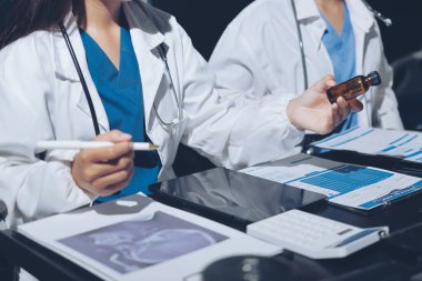 Two doctors and a female nurse meet at a table in the hospital, collaborating on medical tasks using laptops and computers