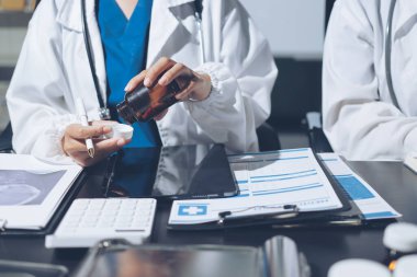 Two doctors and a female nurse meet at a table in the hospital, collaborating on medical tasks using laptops and computers