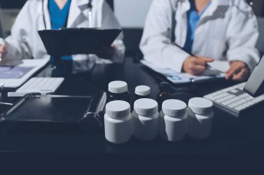 Two doctors and a female nurse meet at a table in the hospital, collaborating on medical tasks using laptops and computers