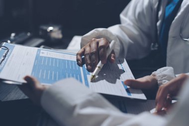 Two doctors and a female nurse meet at a table in the hospital, collaborating on medical tasks using laptops and computers