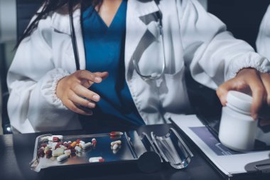 Two doctors and a female nurse meet at a table in the hospital, collaborating on medical tasks using laptops and computers
