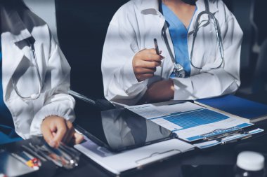 Two doctors and a female nurse meet at a table in the hospital, collaborating on medical tasks using laptops and computers