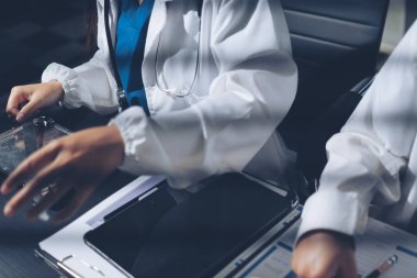 Two doctors and a female nurse meet at a table in the hospital, collaborating on medical tasks using laptops and computers