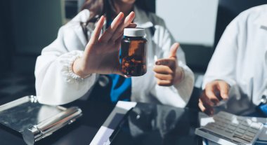 Two doctors and a female nurse meet at a table in the hospital, collaborating on medical tasks using laptops and computers