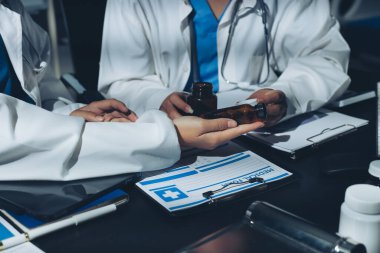 Two doctors and a female nurse meet at a table in the hospital, collaborating on medical tasks using laptops and computers