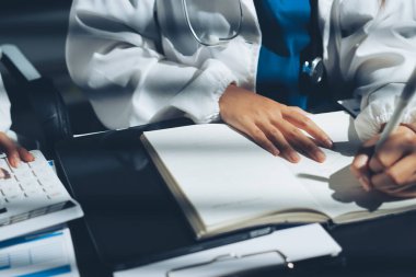 Two doctors and a female nurse meet at a table in the hospital, collaborating on medical tasks using laptops and computers