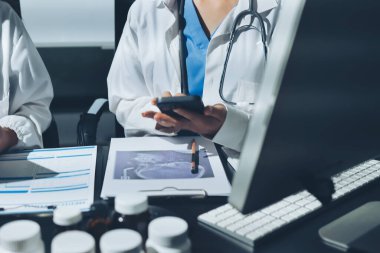 Two doctors and a female nurse meet at a table in the hospital, collaborating on medical tasks using laptops and computers