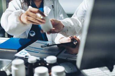 Two doctors and a female nurse meet at a table in the hospital, collaborating on medical tasks using laptops and computers