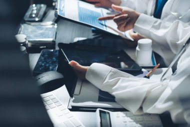 Two doctors and a female nurse meet at a table in the hospital, collaborating on medical tasks using laptops and computers