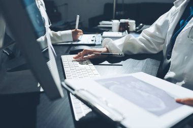 Two doctors and a female nurse meet at a table in the hospital, collaborating on medical tasks using laptops and computers