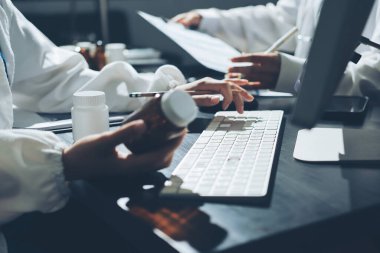Two doctors and a female nurse meet at a table in the hospital, collaborating on medical tasks using laptops and computers