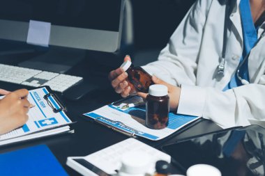 Two doctors and a female nurse meet at a table in the hospital, collaborating on medical tasks using laptops and computers