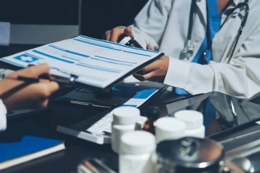 Two doctors and a female nurse meet at a table in the hospital, collaborating on medical tasks using laptops and computers