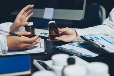 Two doctors and a female nurse meet at a table in the hospital, collaborating on medical tasks using laptops and computers