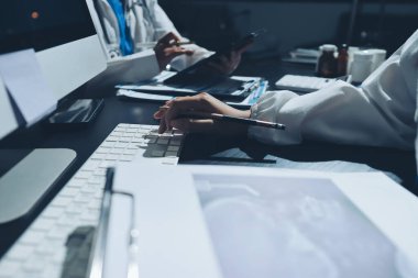Two doctors and a female nurse meet at a table in the hospital, collaborating on medical tasks using laptops and computers
