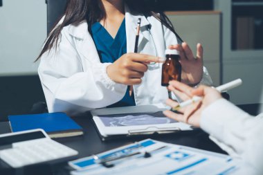 Two doctors and a female nurse meet at a table in the hospital, collaborating on medical tasks using laptops and computers