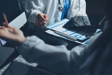 Two doctors and a female nurse meet at a table in the hospital, collaborating on medical tasks using laptops and computers