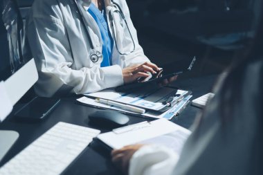 Two doctors and a female nurse meet at a table in the hospital, collaborating on medical tasks using laptops and computers