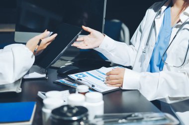 Two doctors and a female nurse meet at a table in the hospital, collaborating on medical tasks using laptops and computers