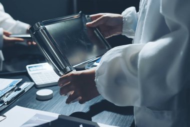 Two doctors and a female nurse meet at a table in the hospital, collaborating on medical tasks using laptops and computers