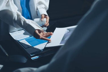 Two doctors and a female nurse meet at a table in the hospital, collaborating on medical tasks using laptops and computers