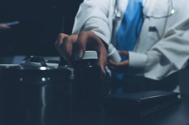 Two doctors and a female nurse meet at a table in the hospital, collaborating on medical tasks using laptops and computers