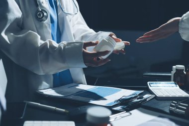 Two doctors and a female nurse meet at a table in the hospital, collaborating on medical tasks using laptops and computers