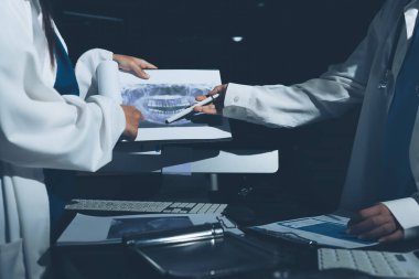 Two doctors and a female nurse meet at a table in the hospital, collaborating on medical tasks using laptops and computers