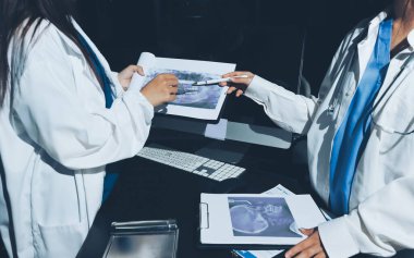 Two doctors and a female nurse meet at a table in the hospital, collaborating on medical tasks using laptops and computers