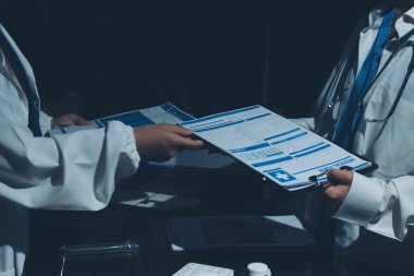 Two doctors and a female nurse meet at a table in the hospital, collaborating on medical tasks using laptops and computers