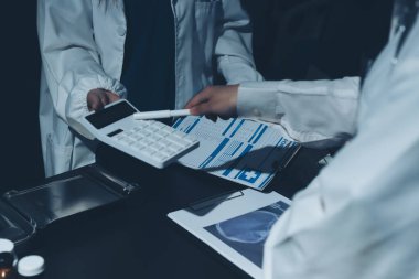 Two doctors and a female nurse meet at a table in the hospital, collaborating on medical tasks using laptops and computers
