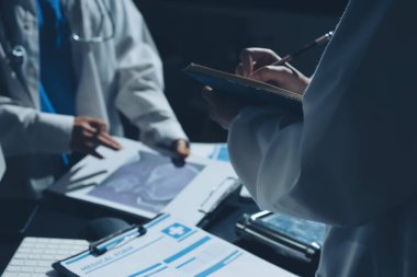 Two doctors and a female nurse meet at a table in the hospital, collaborating on medical tasks using laptops and computers