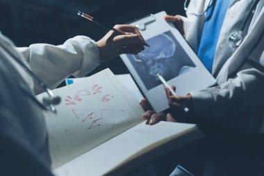 Two doctors and a female nurse meet at a table in the hospital, collaborating on medical tasks using laptops and computers