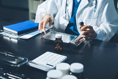 Elinde ilaç şişesi olan kadın doktor hastanın yan etkileri için ilaç kalitesini kontrol ediyor ve hasta bilgilerini hastanede kaydediyor. tıbbi ve sağlık hizmetleri kavramı
