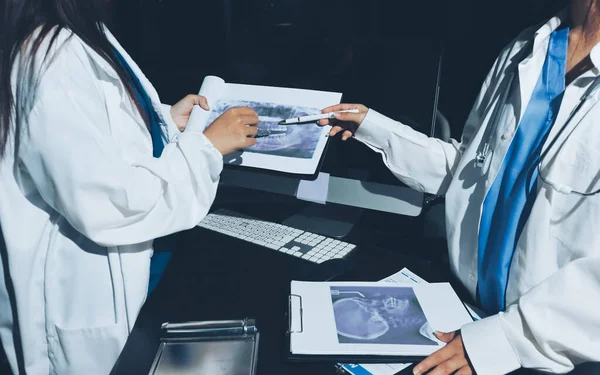 Two doctors and a female nurse meet at a table in the hospital, collaborating on medical tasks using laptops and computers