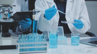 Laboratuvar çalışanı üniformalı ve laboratuarda mikroskop takmış koruyucu kıyafetli.