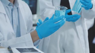 Beyaz önlüklü bir bilim adamı cam bir şişe tutuyor ve bir tüpe bakıyor.