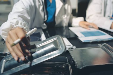 Two doctors and a female nurse meet at a table in the hospital, collaborating on medical tasks using laptops and computers