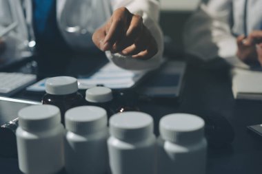 Two doctors and a female nurse meet at a table in the hospital, collaborating on medical tasks using laptops and computers