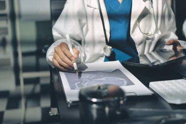 Two doctors and a female nurse meet at a table in the hospital, collaborating on medical tasks using laptops and computers