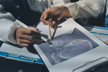Two doctors and a female nurse meet at a table in the hospital, collaborating on medical tasks using laptops and computers