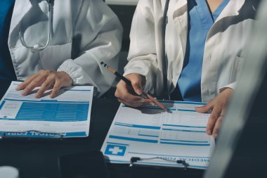 Two doctors and a female nurse meet at a table in the hospital, collaborating on medical tasks using laptops and computers