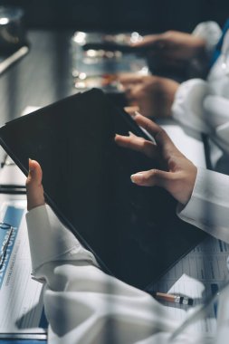 Two doctors and a female nurse meet at a table in the hospital, collaborating on medical tasks using laptops and computers